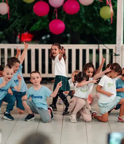 Children dancing on an outdoor summer stage, all pointing a finger upwards