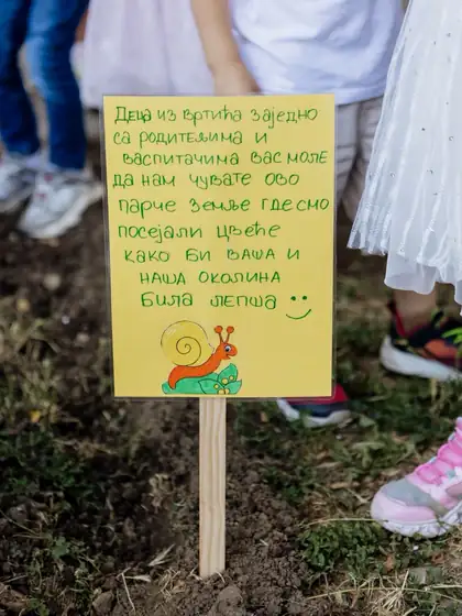 Handwritten yellow sign on a wooden stake in a freshly dug garden bed
