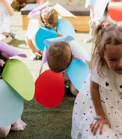 Children in colourful handmade paper hats crouching on artificial grass in the yard