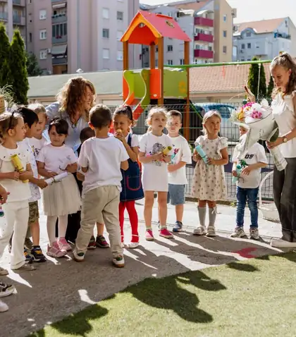 Children in the kindergarten yard holding rolled-up diplomas, with two teachers