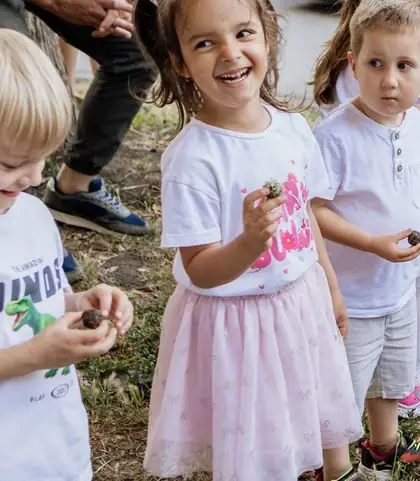 Laughing girl with pigtails and a pink tutu holding a clump of soil