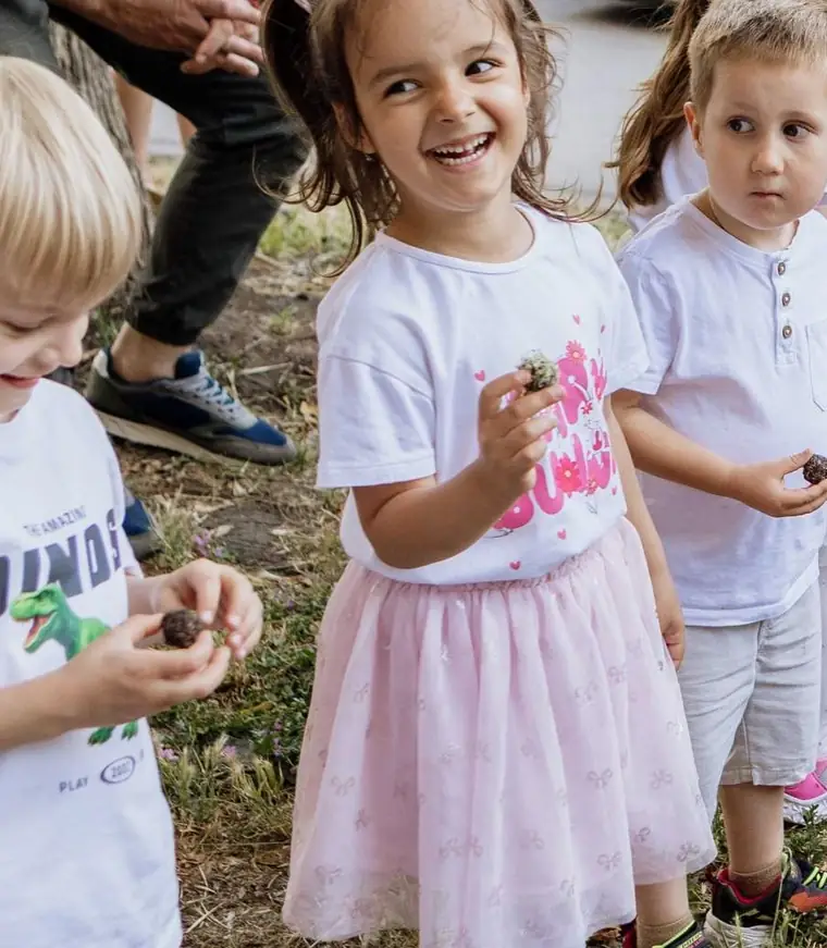 Nasmejana devojčica sa kikicama i roze tutu suknjicom drži grudvicu zemlje