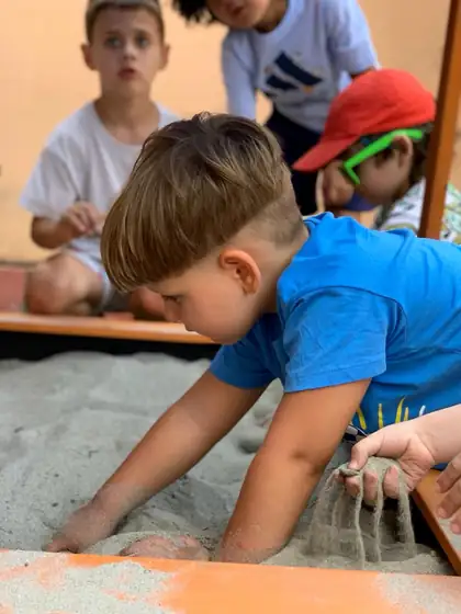 Boy in a blue T-shirt kneeling by the sandpit, sifting sand