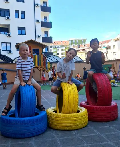 Three boys sitting on painted tyres in the yard, two of them waving