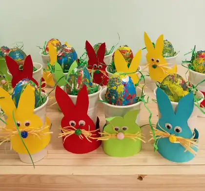 Easter bunnies made from coloured paper and plastic cups on a wooden shelf