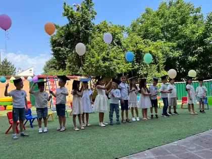 End-of-year performance in the yard, some children wearing graduation caps