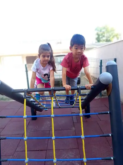 A girl and a boy climbing a blue and yellow rope net on the playground