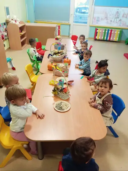 Toddlers at a long low table with baskets of autumn leaves and fruit