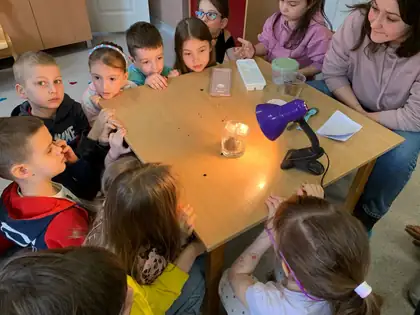 Children watching a water-cycle experiment warmed by a desk lamp