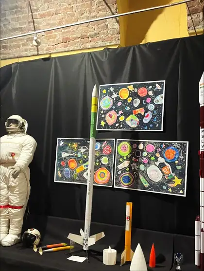 Space museum display with a spacesuit, model rockets and children's drawings of planets