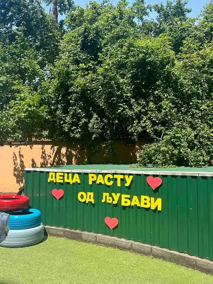 Yellow letters on the green yard fence reading “Children grow from love”, with red hearts