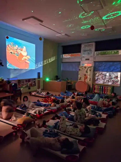 Children lying on mats in a darkened room, watching a cartoon on a screen